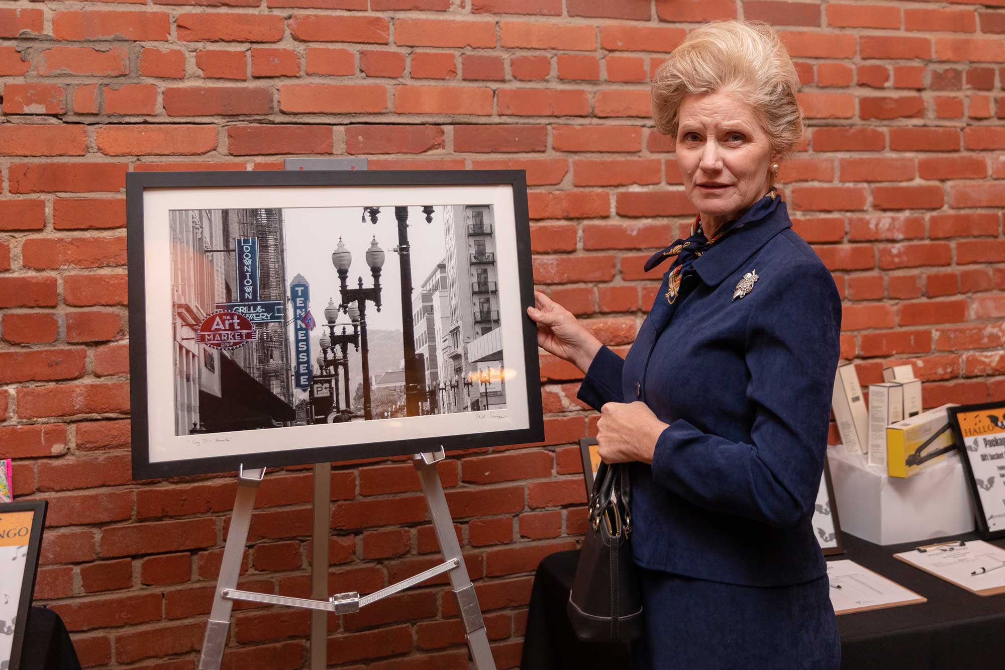 A woman in a suit standing next to a framed photograph.