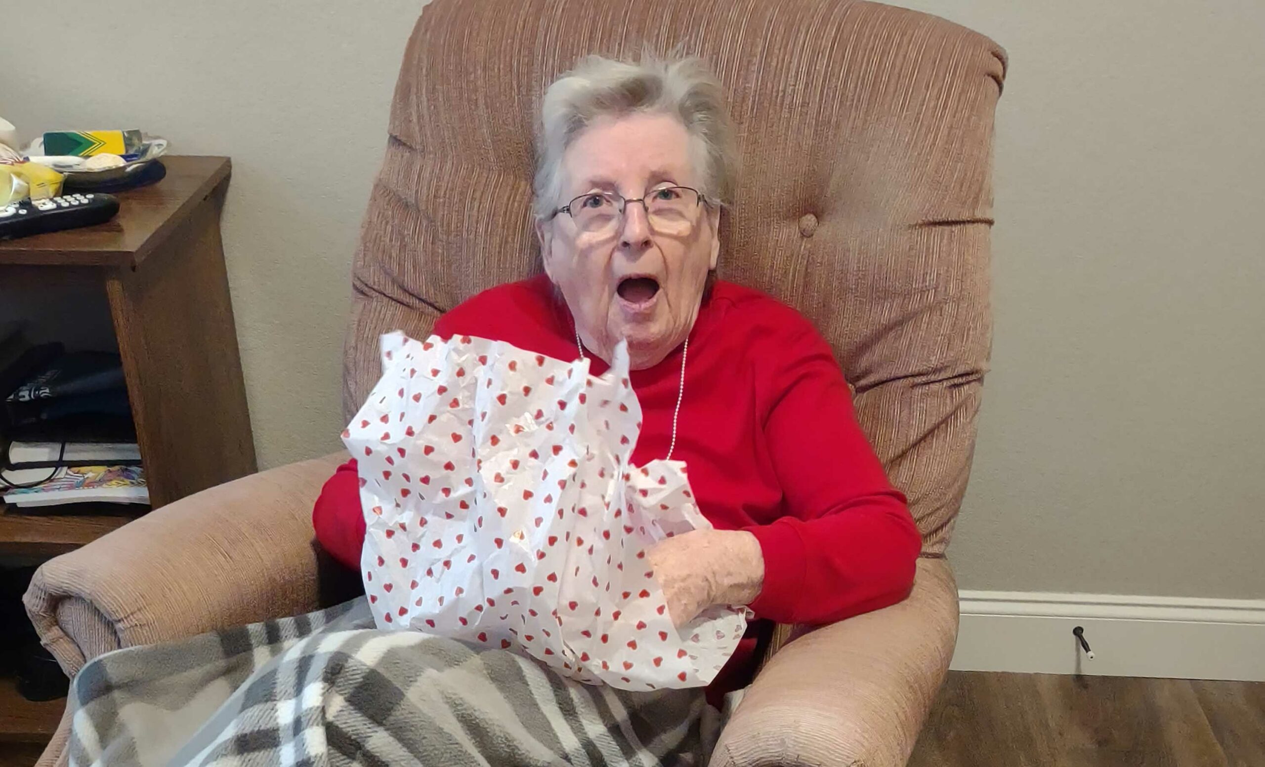An elderly woman is sitting in a chair and holding a gift.