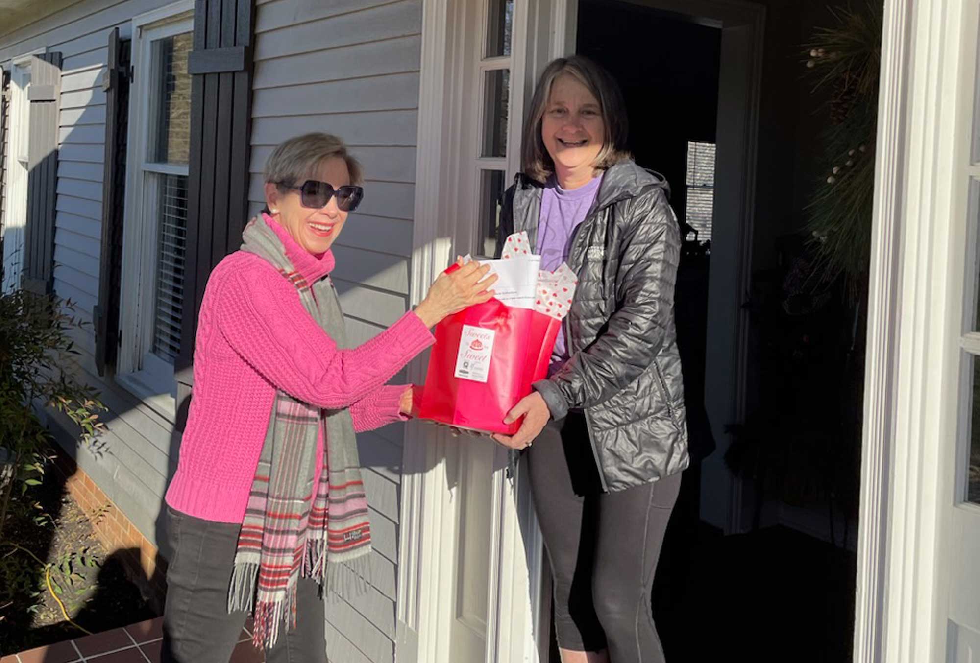 Two women standing in front of a house with a red gift bag.